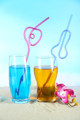 Glasses of cocktails on sand, on bright background