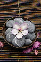 Fototapeta na wymiar Bowl of spa stone with orchid and petals on bamboo mat
