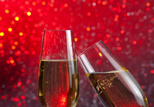 two champagne flutes with gold bubbles on red light bokeh