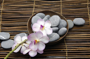 orchid with gray stones in bowl  on bamboo mat
