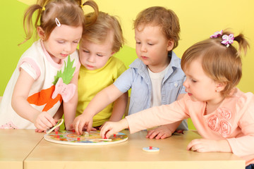 Two boys and two girls doing together wooden puzzle