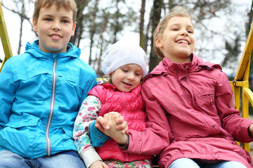 Naklejka premium Cheerful boy and two girls in bright jackets on swings