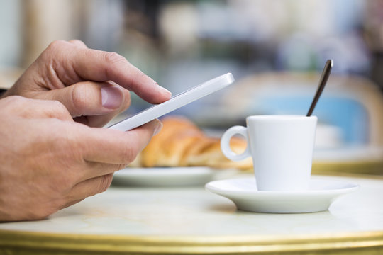 Man using a cell phone on cafe terrace, croissant and coffee