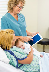 Mature Nurse Explaining Reports On Tablet To Woman With Babygirl