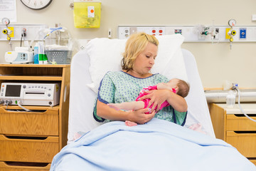 Mother Looking At Newborn Baby Girl While Sitting On Bed