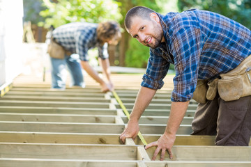 Carpenter Measuring Wood With Tape While Coworker Assisting Him