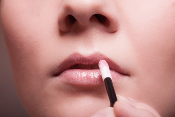 Naklejka premium Makeup. Girl applying lipgloss lipstick on lips. Part of face.