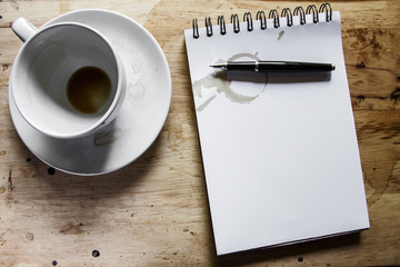 Coffee cup, spiral notebook and pen on the wooden table backgrou