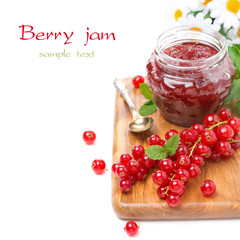 berry jam in a glass jar and fresh red currants on board