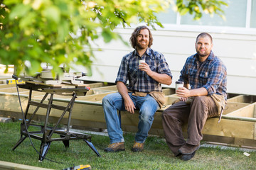 Workers Holding Disposable Cups While Sitting On Wooden Frame