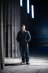 young man in leather coat posing at night against big columns