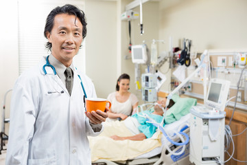 Doctor Holding Coffee Cup With Patient Resting On Bed