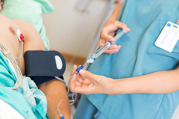 Nurse Injecting Dosage In IV Tube Attached To Patient