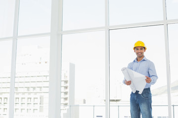 Young architect in yellow hard hat with blueprint in office