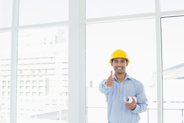 Architect in hard hat with blueprint gesturing thumbs up in offi