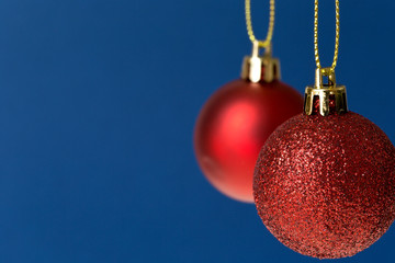 Two different red glitter ornaments on blue background.