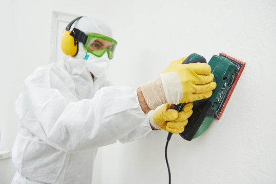 worker with sander at wall filling