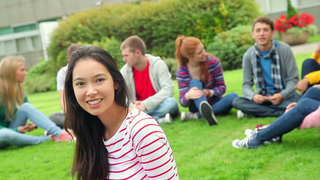 Student smiling at camera with friends behind her on grass