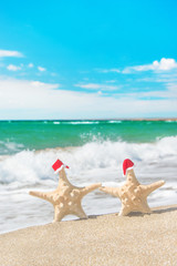 Fototapeta na wymiar Sea-stars couple in santa hats walking at sea beach. New Years d