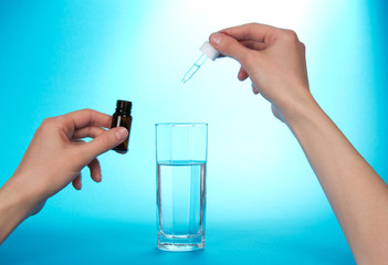 The hand, dripping medical drops in glass with water