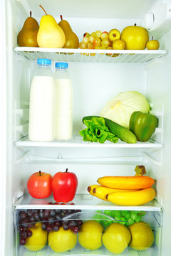 Milk bottles, vegetables and fruits in open refrigerator.