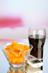 Chips in bowl, cola and TV remote on bright background