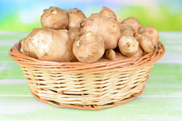 Topinambur roots in wicker basket on table on light background
