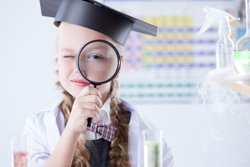 Smiling schoolgirl looks through magnifying glass