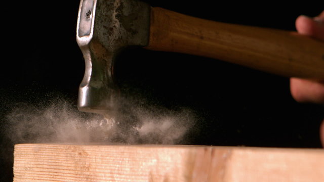 Hammer hitting a nail into wooden plank