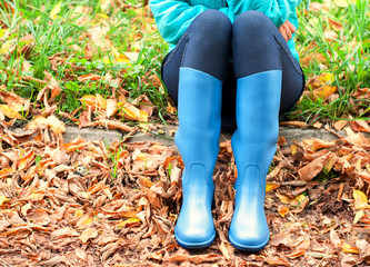 Girl with blue rubber boots sitting on the ground