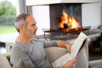 Mature man relaxing by fireplace with newspaper