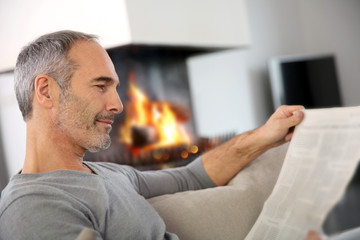 Mature man relaxing by fireplace with newspaper