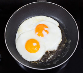 top view of two fried eggs in frying pan