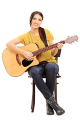 Young female musician on a chair holding an acoustic guitar