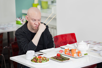 Obraz na płótnie Canvas Man with surprised face eats sushi in cafe