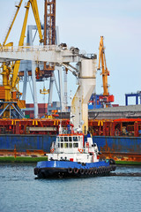 Tugboat assisting bulk cargo ship to harbor quayside