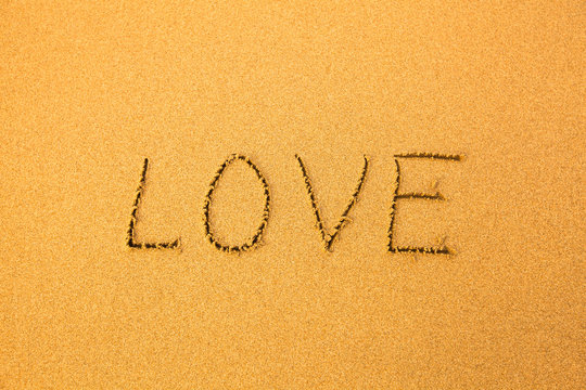 Love - text written by hand in sand on a beach.