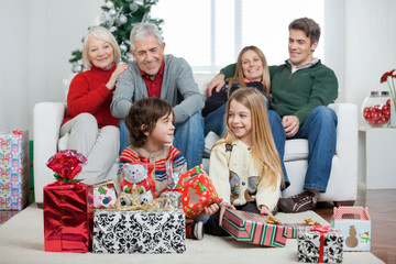 Children With Christmas Presents While Family Sitting On Sofa