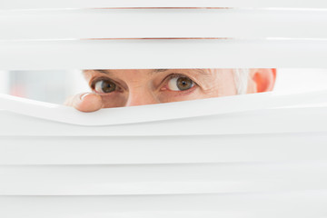Close-up portrait of a businessman peeking through blinds