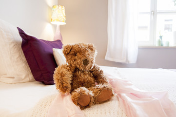 Teddybär auf Bett vor Fenster