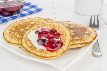 Fresh baked pancakes on plate with cream and red berry sauce