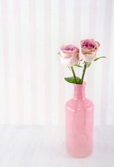 Pink roses in a glass bottle on wooden background