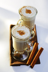 Two mugs of frothy hot chocolate with cinnamon