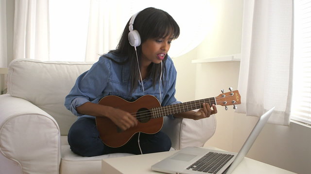 Black girl learning to play ukulele with laptop computer