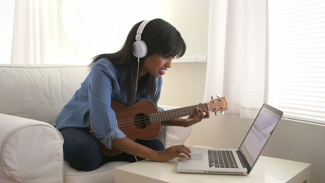 Black girl recording song on ukulele with laptop