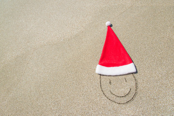 Santa Claus hat and smiley face on seashore against waves and bl
