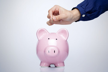 Female hand putting coin into a piggy bank over gray background