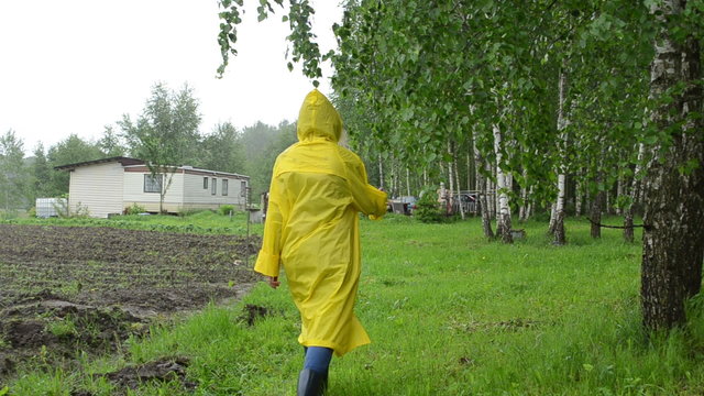 Woman in waterproof coat near birch tree and small garden house