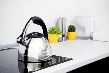 Steel kettle in modern kitchen with induction stove - obrazy, fototapety, plakaty