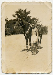 CIRCA 1945: Young man in shorts hugging a horse